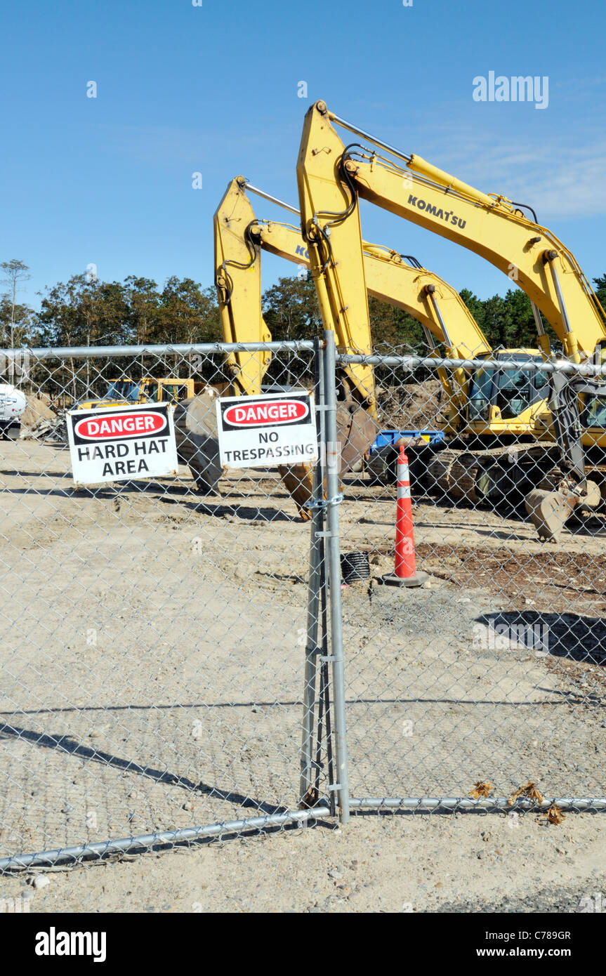 Baustelle mit schwerem Gerät von Metallzaun mit Warnung, Gefahr und Schutzhelm Zeichen umgeben. USA Stockfoto