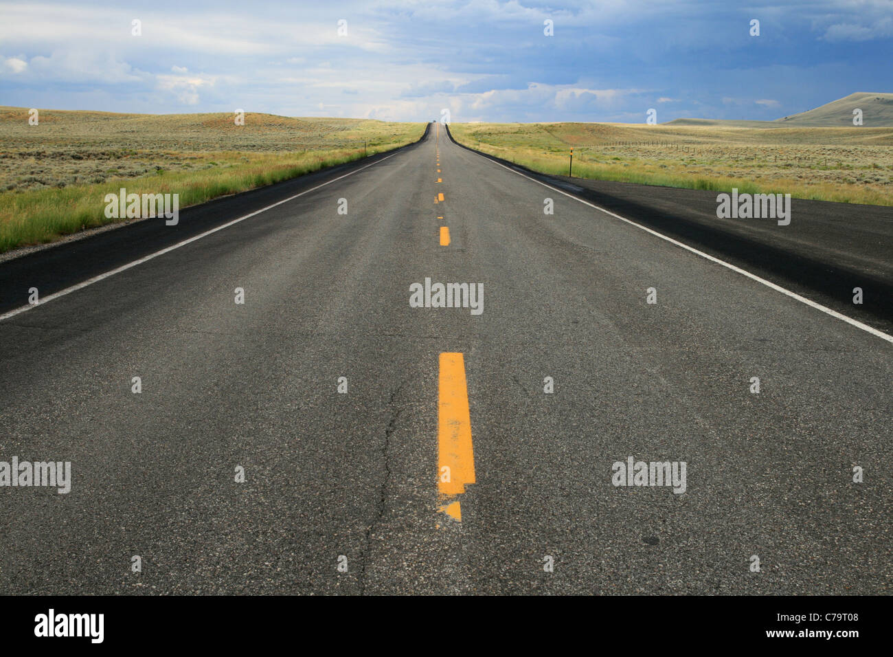 a car crests the distant hill on an empty road in Wyoming Stockfoto