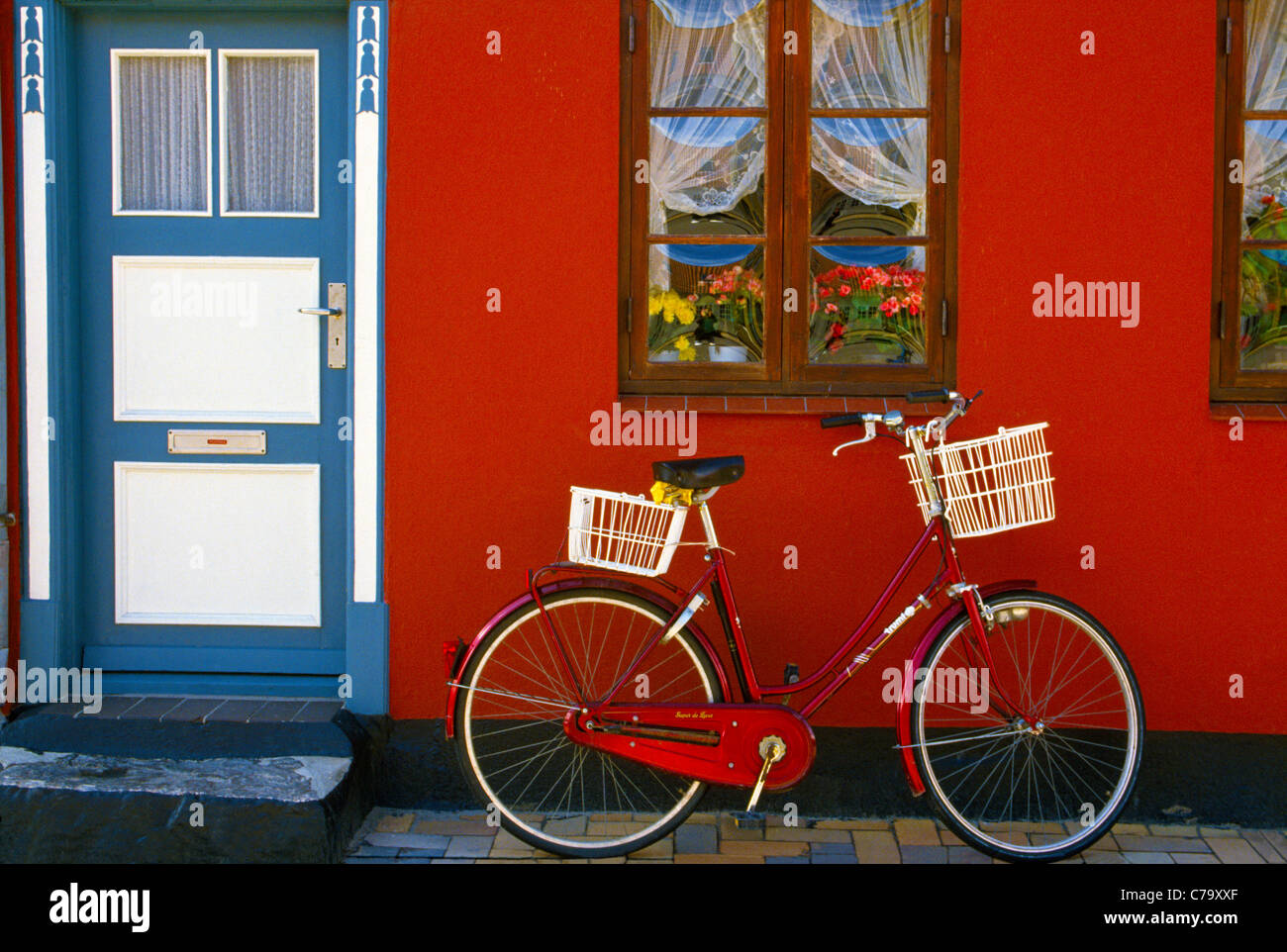 über. Ein rotes Fahrrad vor einer roten Wand geparkt und eine blau-weiße Tür eines Hauses macht eine bunte Straße Tableau in Kerteminde, Dänemark. Stockfoto