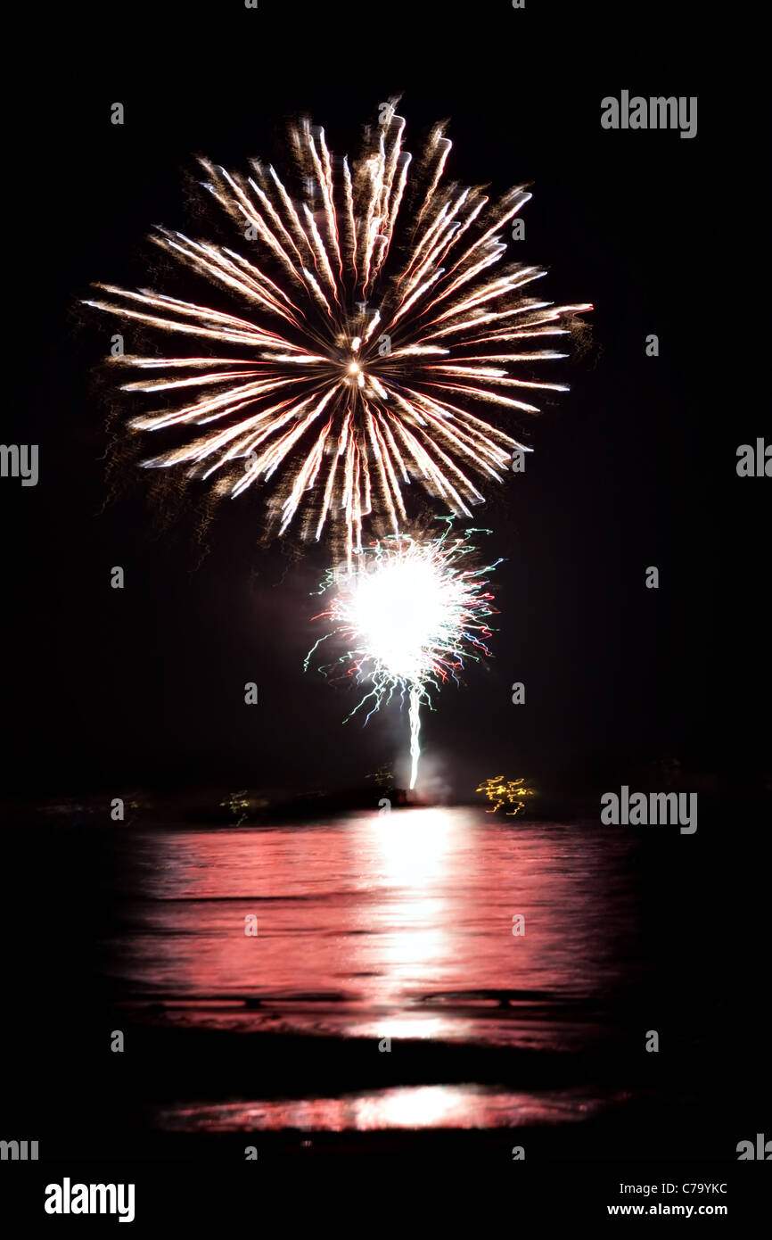 Schönen Feuerwerk über den dunklen Nachthimmel über dem Wasser reflektiert. Stockfoto