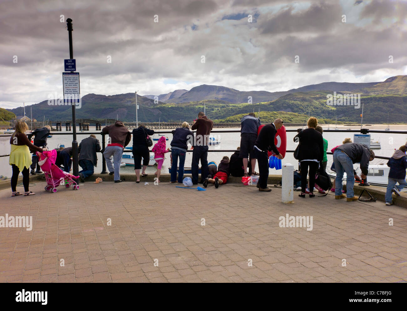 Familien, beugte sich über Geländer am Rande des Meeres, Krabben fischen zu fangen. Barmouth Hafen, Berge, Schiffe im Hintergrund, Stockfoto