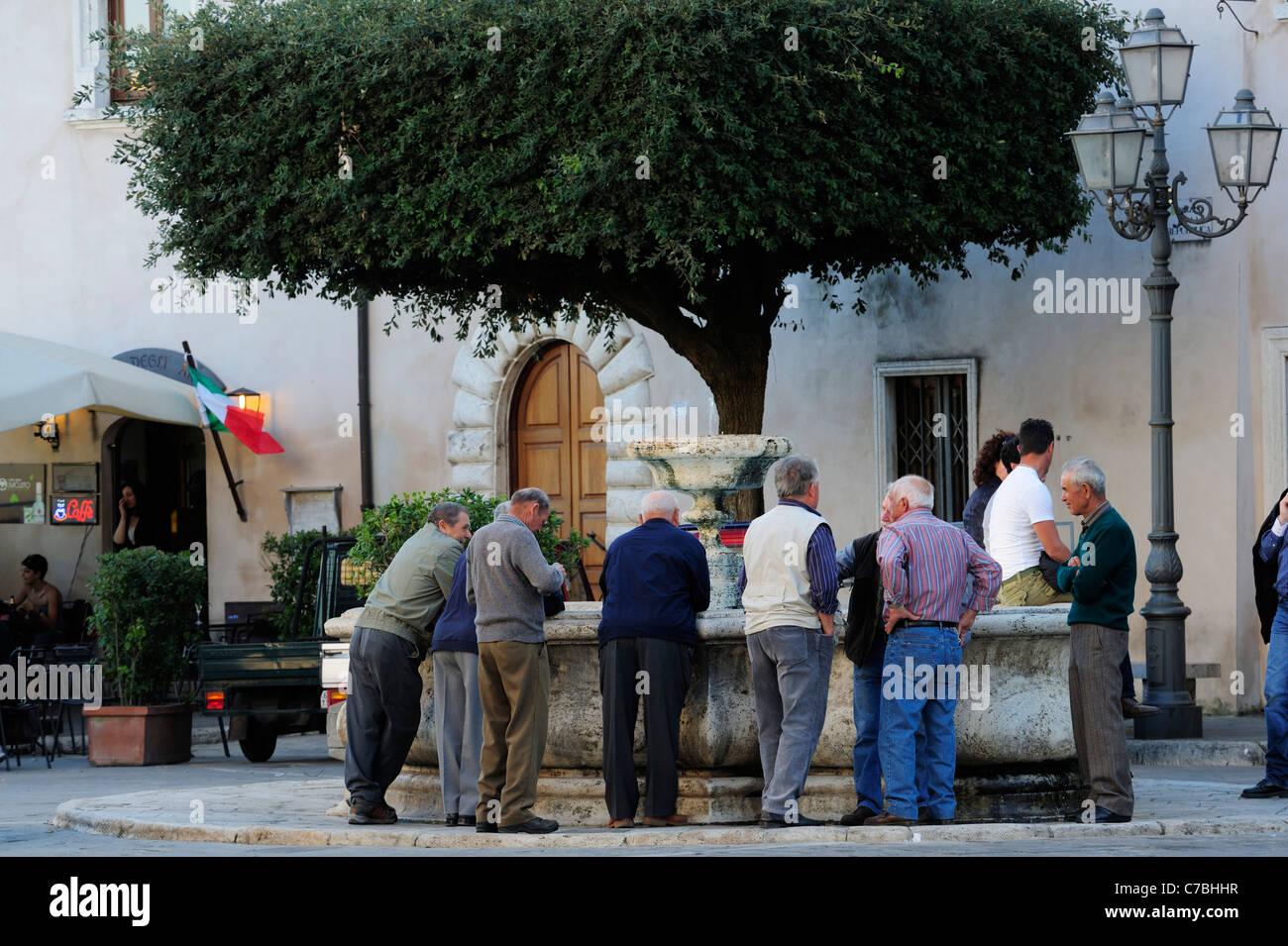 Männer stehen um den Brunnen herum und im Chat, Pitigliano, Toskana, Italien Stockfoto