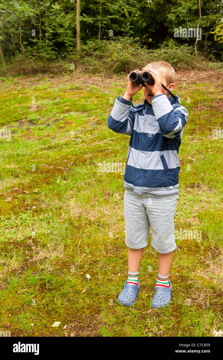 Ein sieben Jahre alter Junge Vogelbeobachtung mit dem Fernglas in Fairhaven Garten Wald und Wasser im Süden Walsham, Norfolk, Großbritannien Stockfoto