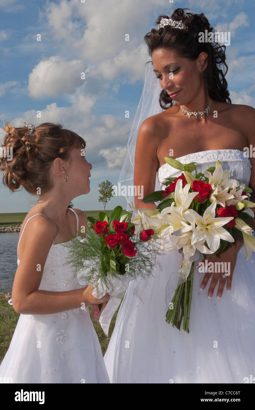 Ein Porträt des frisch vermählte Braut und ein Blumenmädchen suchen ineinander Augen mit blauem Himmel und weißen geschwollenen Wolken im Hintergrund Stockfoto