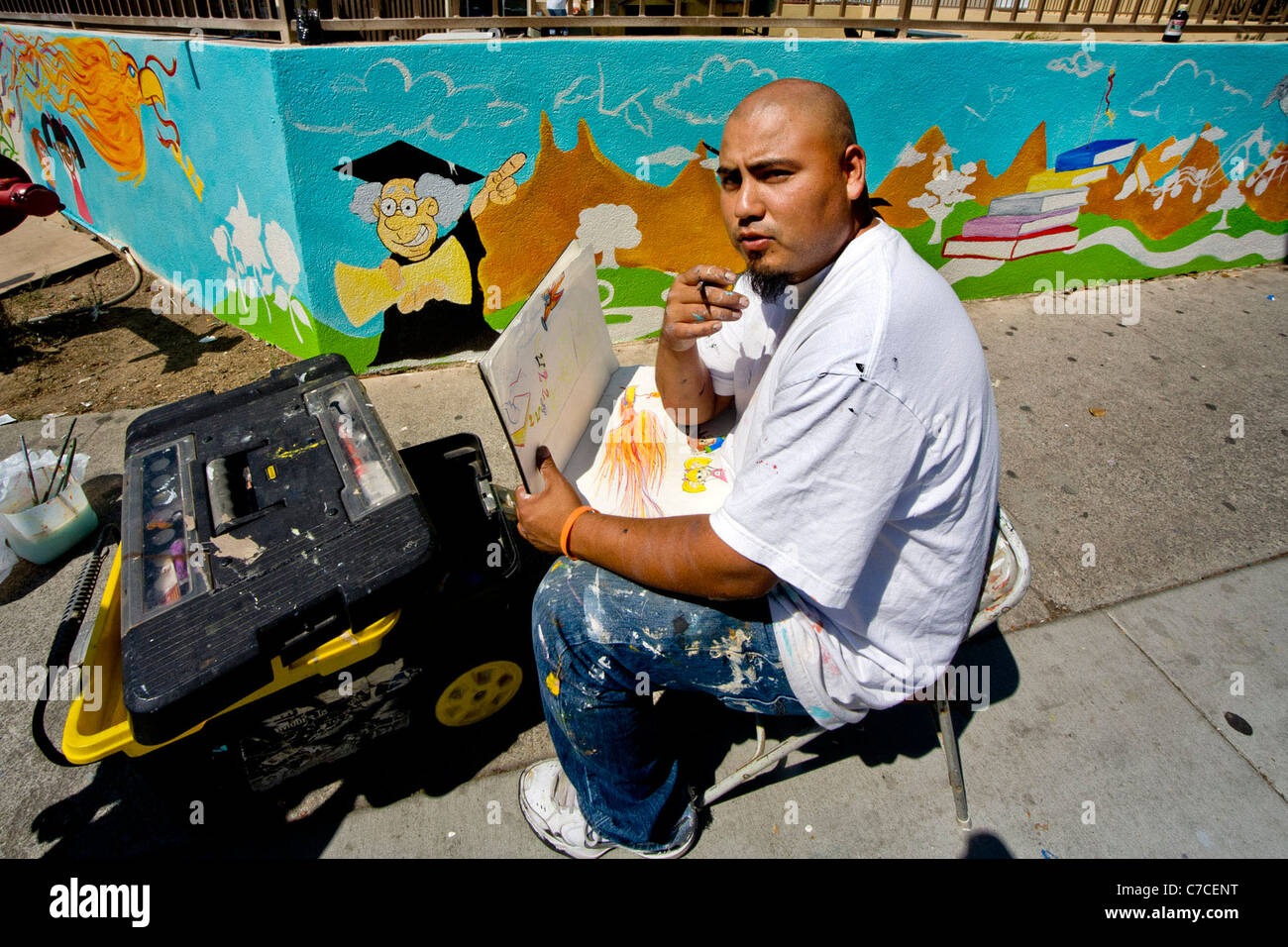 Ein freiwilliger Künstler Hispanic prüft seine ursprüngliche Zeichnung gegen die fertige Arbeit auf einem Wandbild als Teil einer Nachbarschaft Deco Stockfoto