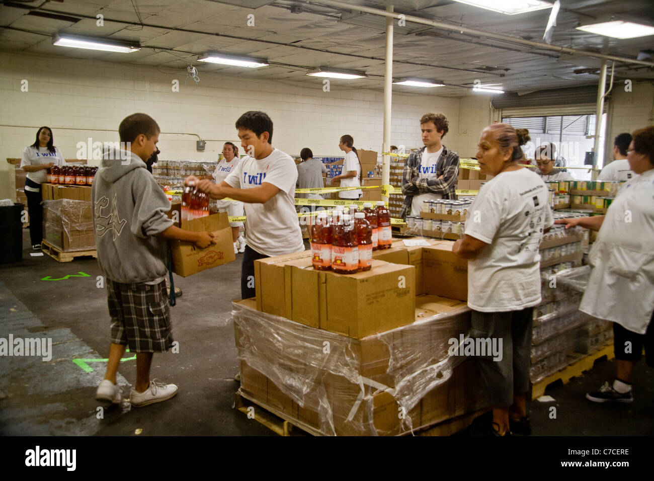 Hispanic und kaukasischen Freiwilligen geben Essen mit einem jungen Mann an eine Wohltätigkeitsorganisation Lebensmittelvertrieb in Santa Ana, CA. Hinweis Logo T-shirt. Stockfoto