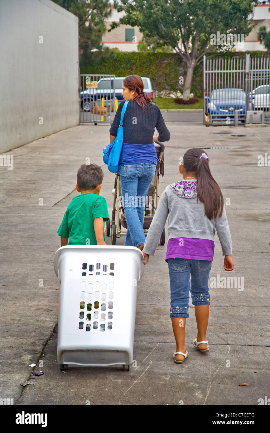 Eine junge spanische Mutter und ihre drei Kinder tragen nach Hause gespendete Lebensmittel bei einer Charity-Verteilung in Santa Ana, CA. Stockfoto