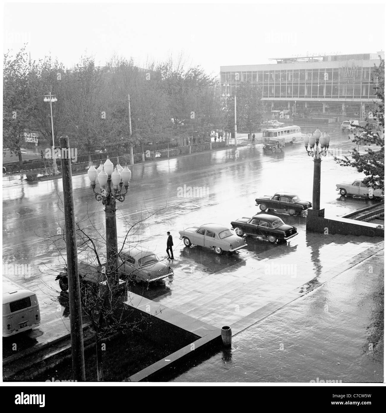 Historisches Bild aus Russland, 50er Jahre. Autos der damaligen Zeit parkten an einem nassen Abend in der ehemaligen Sowjetunion vor einem Gebäude. Stockfoto