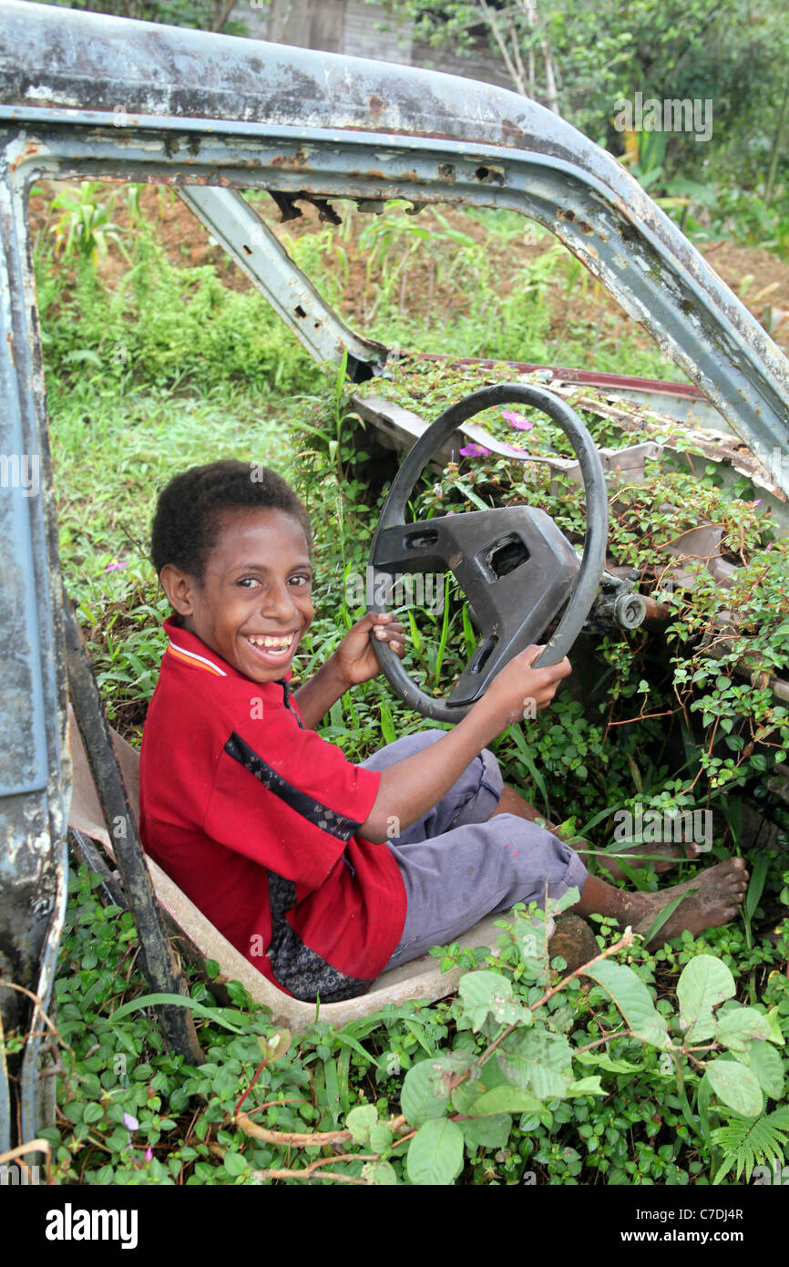 Junge in einer verlassenen überwucherten rostigen Autowrack, Papua-Neu-Guinea Stockfoto