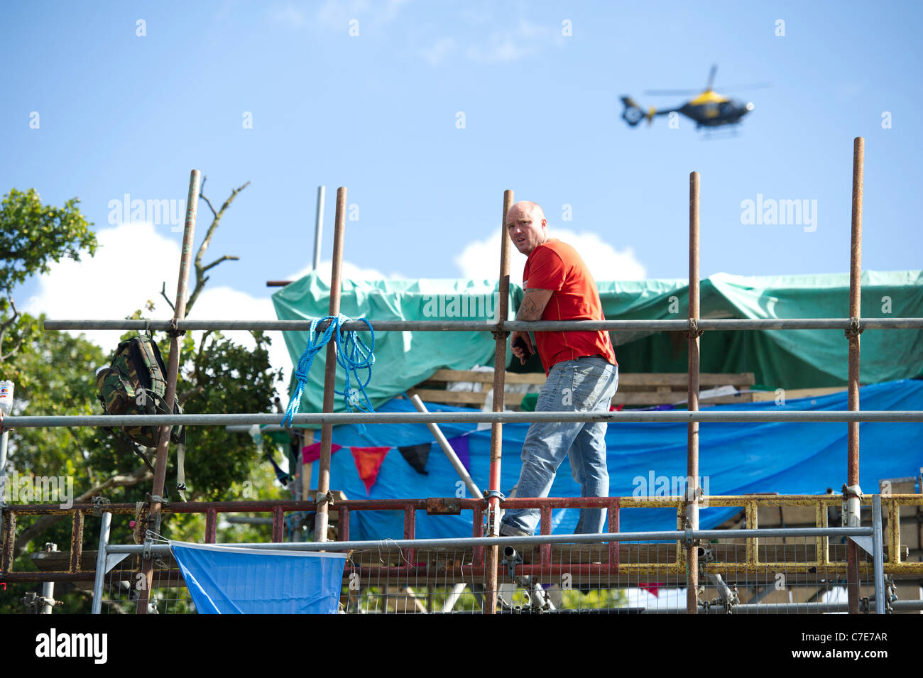 Dale Farm Räumung. Mann auf Gerüst überragen verbarrikadiert Eintrag zu Reisenden Website als Polizei-Hubschrauber-Monitore-Situation. Stockfoto