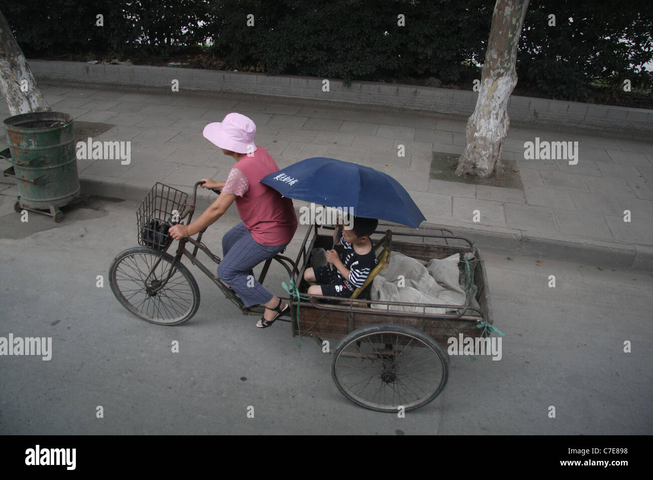 Eine Frau mit einem Dreirad-Wagen tragen einen kleinen Jungen mit einem Sonnenschirm in Jingzhou, China Stockfoto