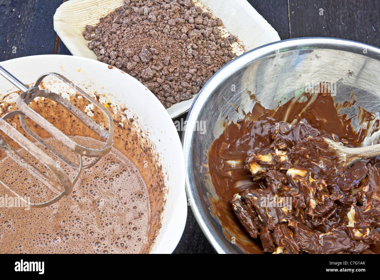 eine Schüssel mit Schokoladenkuchen, eine Schale mit geschmolzener Schokolade und Butter und eine Schüssel mit gehackte Schokolade Stockfoto