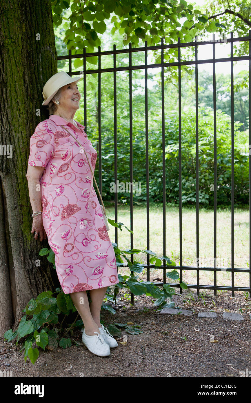 Ältere Frau glücklich gelehnt Baum im park Stockfoto