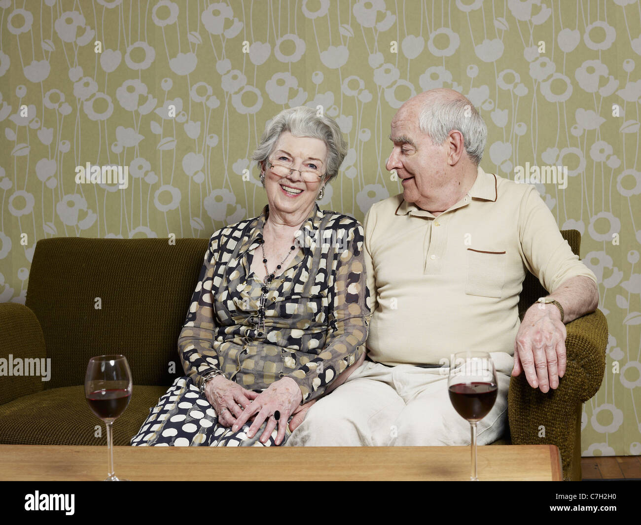 Älteres Paar entspannt auf Couch mit zwei Gläser Wein auf dem Tisch Stockfoto