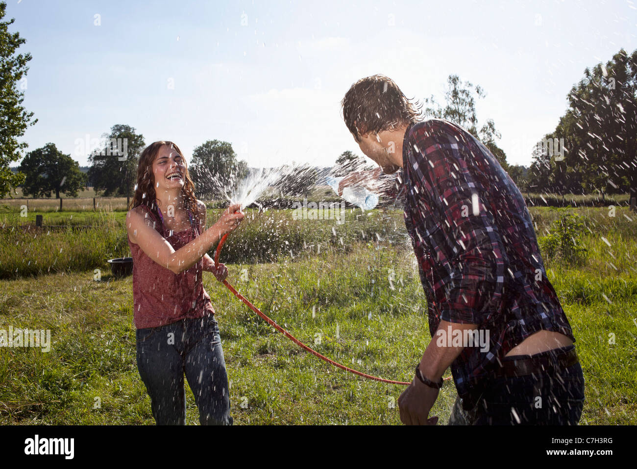 Mädchen-Sprays Kerl mit Schlauch auf Feld Stockfoto