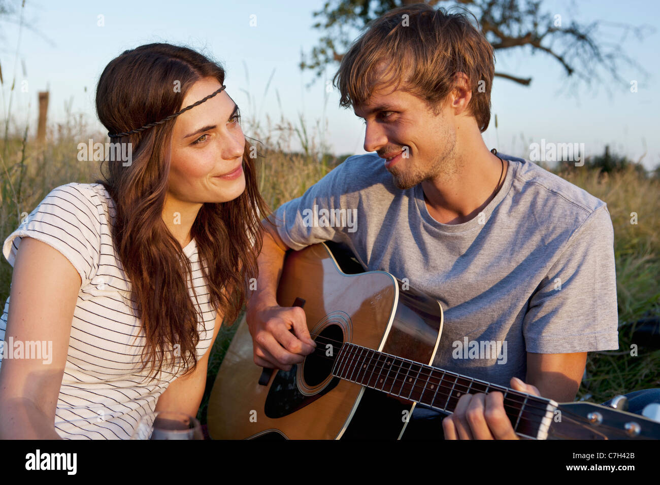Mann spielt Gitarre, seine Freundin im Feld Stockfoto
