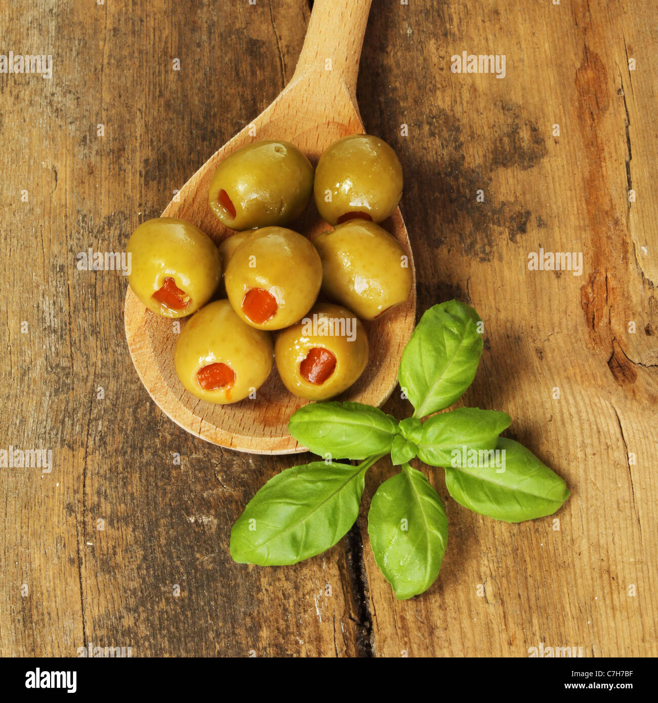 Oliven mit einem Zweig Basilikum in einem Holzlöffel auf einem Hintergrund von alten geknackt und verwitterte Holz Stockfoto