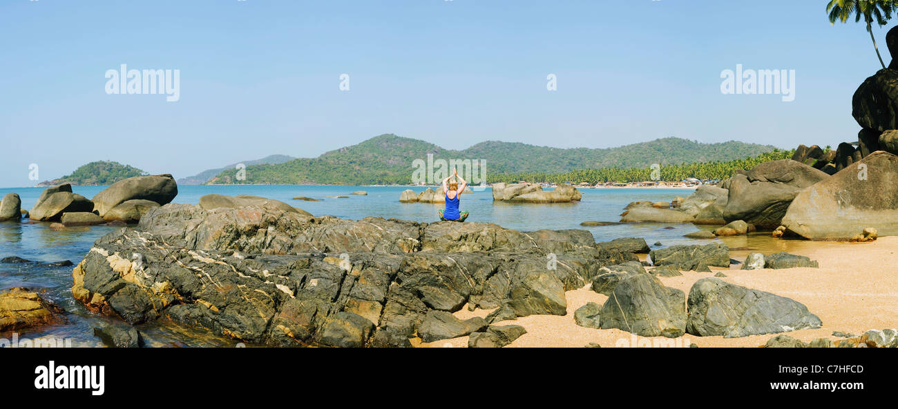 Panoramablick auf eine Frau tun Meditation Yoga auf den Felsen an einem Strand in einem tropischen Ambiente Stockfoto