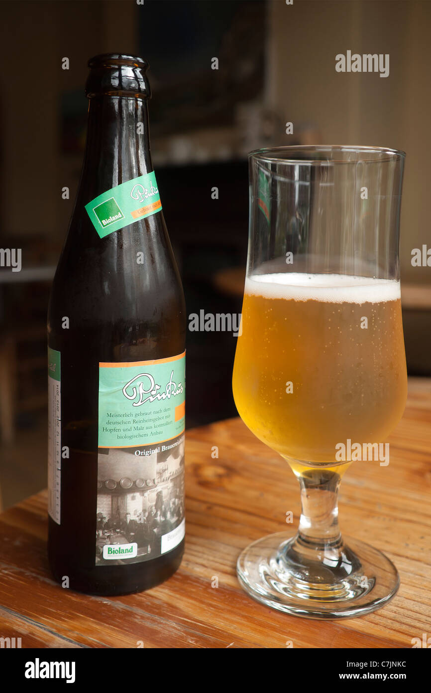 Eine Flasche deutschen Lager und eine halbe volle Glas in einem englischen Vegetarian restaurant Stockfoto
