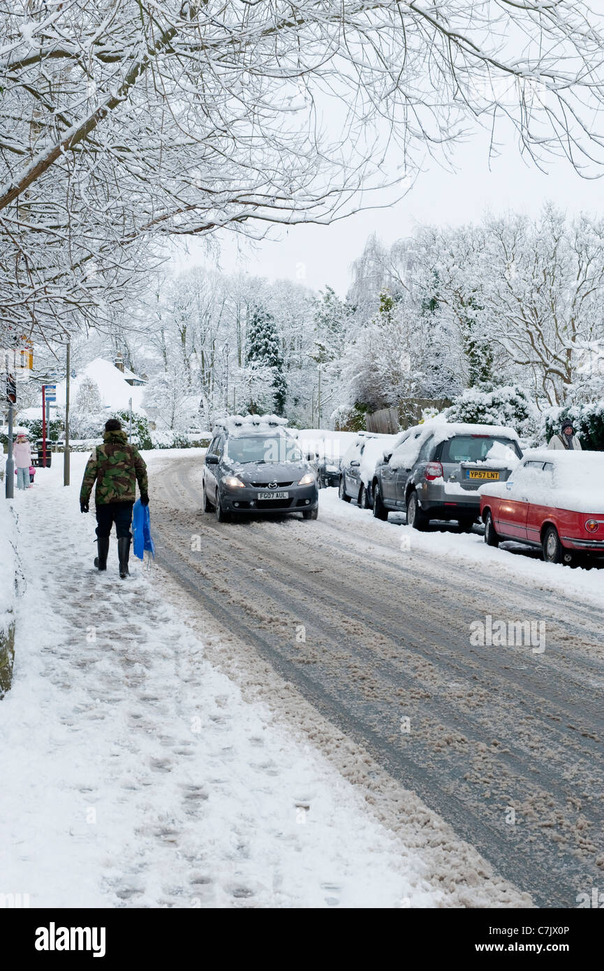 Winter Village Street (schneebedeckte Fahrbedingungen, Autos auf der Straße, Fußgänger zu Fuß, schneebedeckte Bürgersteig) - Burley in Wharfedale, England, GB, Großbritannien. Stockfoto