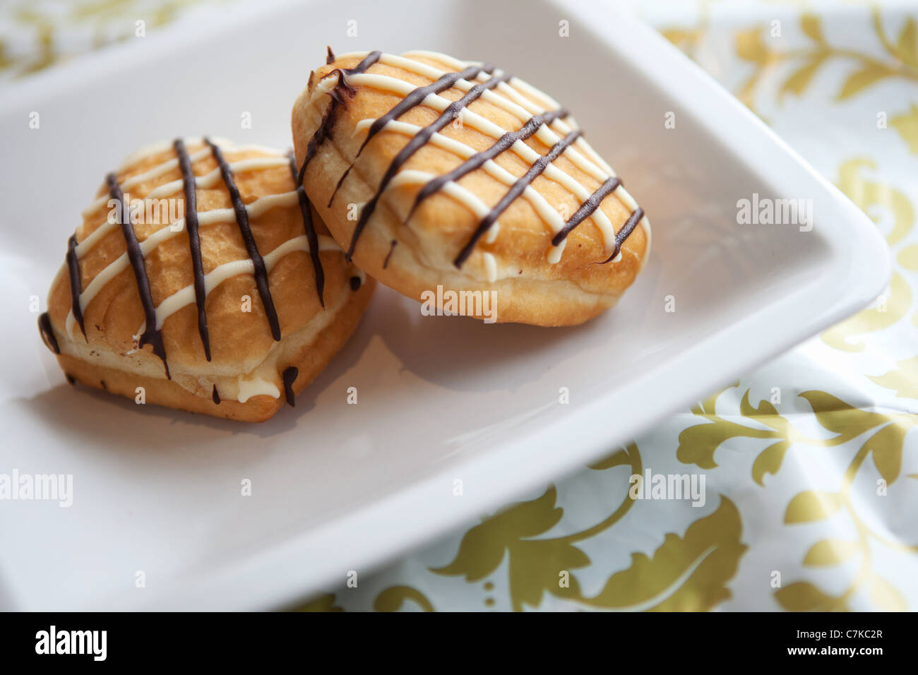 Zwei Creme Donuts auf einem weißen Teller, gegen einen gemusterten Tischdecke Stockfoto