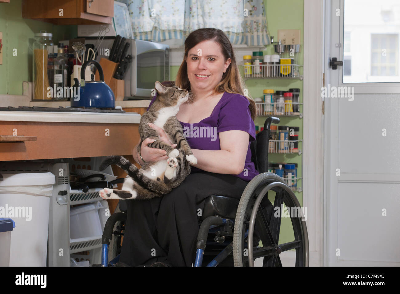 Frau mit Spina Bifida in einem Rollstuhl spielen mit ihrer Katze in ihrer Küche Stockfoto