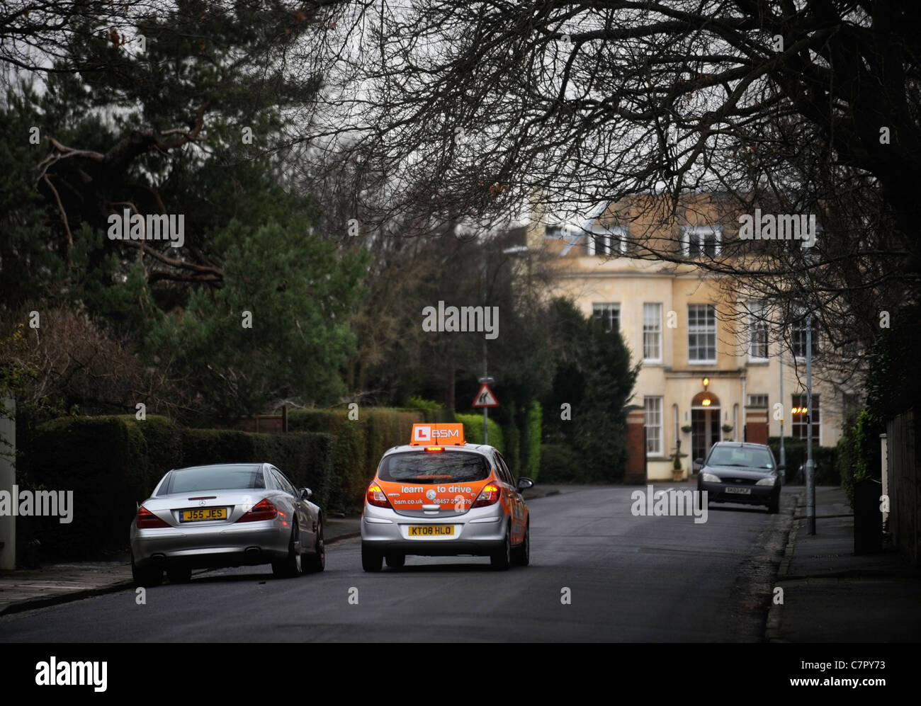 BSM Instruktoren Steuerwagen rundet einen stationäre Mercedes in einem in der Regel Vorort Straße in England UK Stockfoto