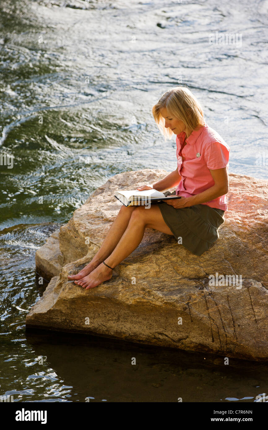 Einsame Frau sitzt auf einem Felsen in einem Fluss, ein Buch zu lesen Stockfoto Einsame Frau sitzt auf einem Felsen in einem Fluss, ein Buch zu lesen Stockfoto