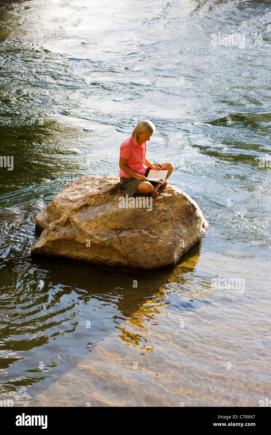 Einsame Frau sitzt auf einem Felsen in einem Fluss, ein Buch zu lesen Stockfoto Einsame Frau sitzt auf einem Felsen in einem Fluss, ein Buch zu lesen Stockfoto