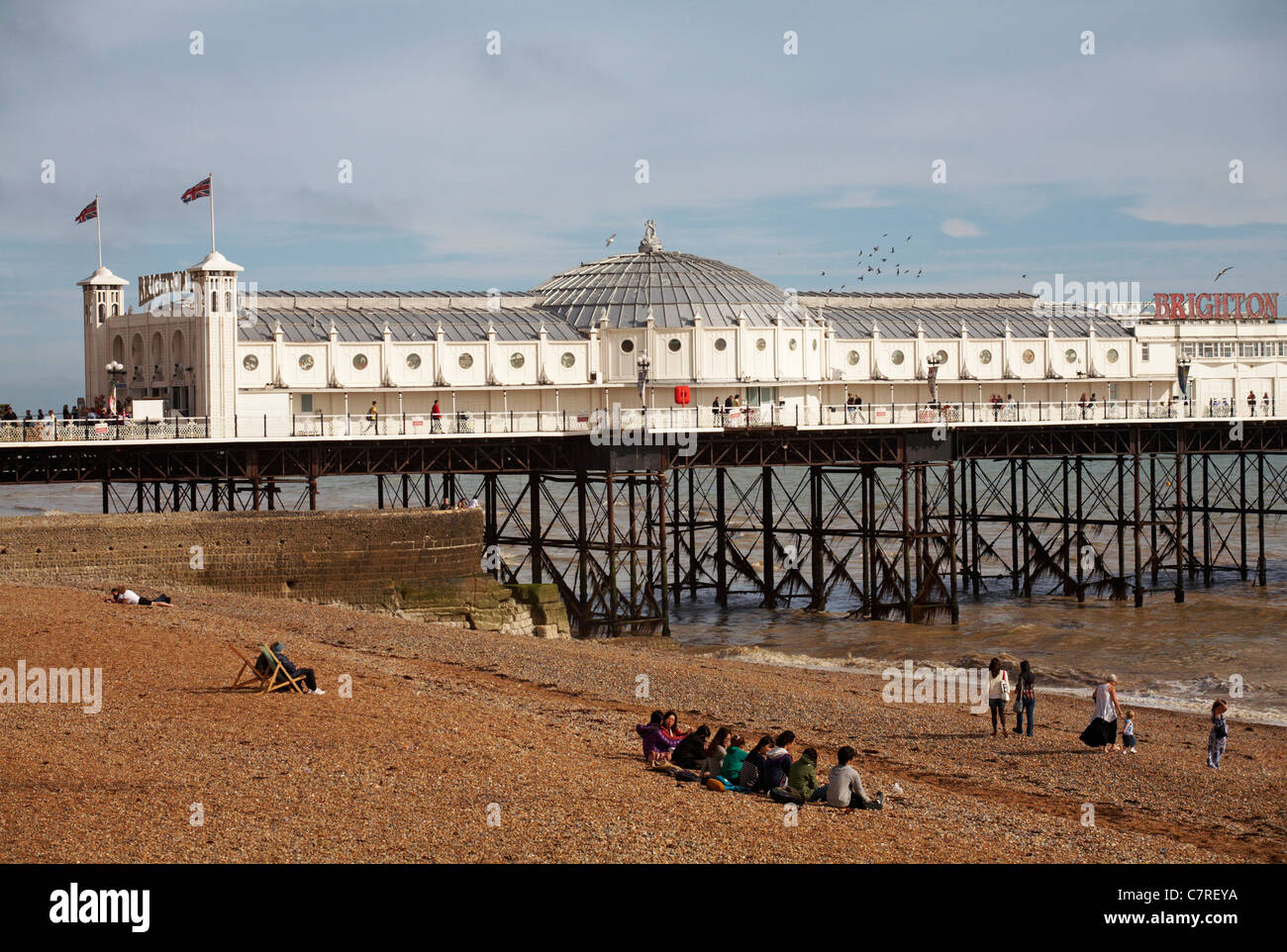 Ausländische Studenten sitzen am Strand von Brighton Pier im September Stockfoto