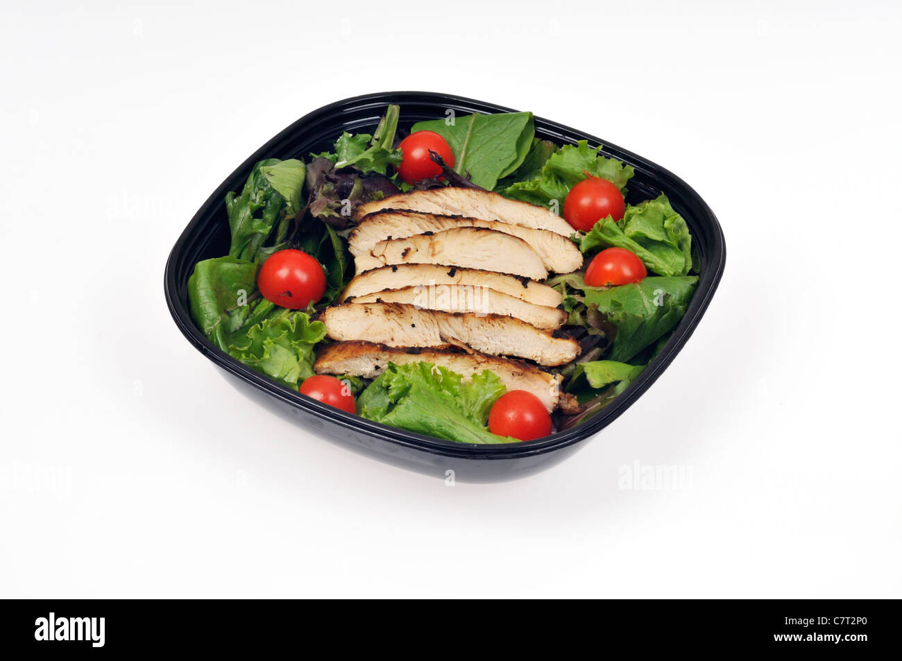 Streifen von gegrilltem Hähnchen auf einem Bett von Salat und Kirschtomaten in einem Salat in schwarzen Behälter auf weißem Hintergrund Ausschnitt. Stockfoto