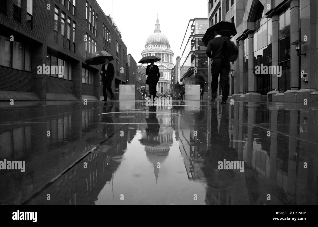 Fußgänger zu Fuß entlang einer regnerischen Peter Hill Weg von St. Pauls Cathedral, City of London, UK Stockfoto