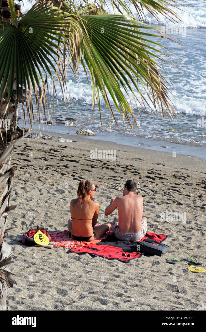 Paar am Strand, Marbella, Costa del Sol, Provinz Malaga, Andalusien, Spanien, Westeuropa sitzt. Stockfoto