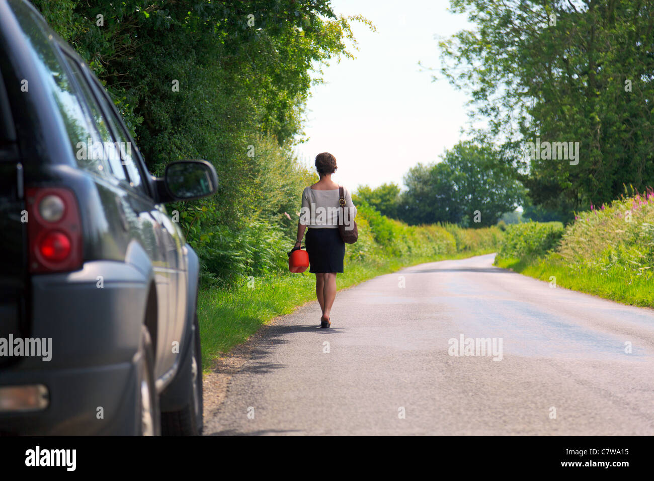 Foto von einer Frau, die ist Fahrzeug ist kaputt gegangen zu Fuß entlang einer Landstraße mit einer Ersatz-Brennstoff-Dose in der Hand. Stockfoto