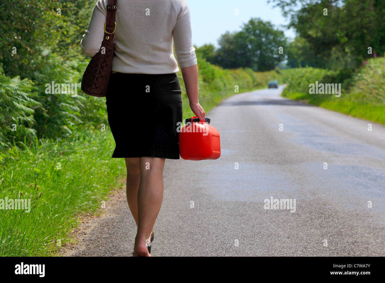 Foto von einer Frau, die ist Fahrzeug ist kaputt gegangen zu Fuß entlang einer Landstraße mit einer Ersatz-Brennstoff-Dose in der Hand. Stockfoto