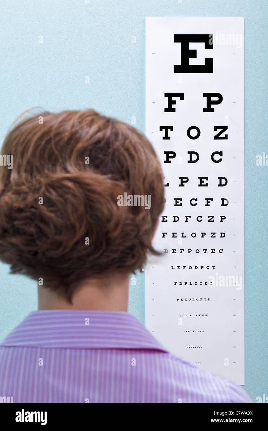 Foto von einer Frau beim Optiker, die ihr Sehvermögen getestet, mit einem Auge Diagramm um zu sehen, ob sie eine Brille braucht. Stockfoto