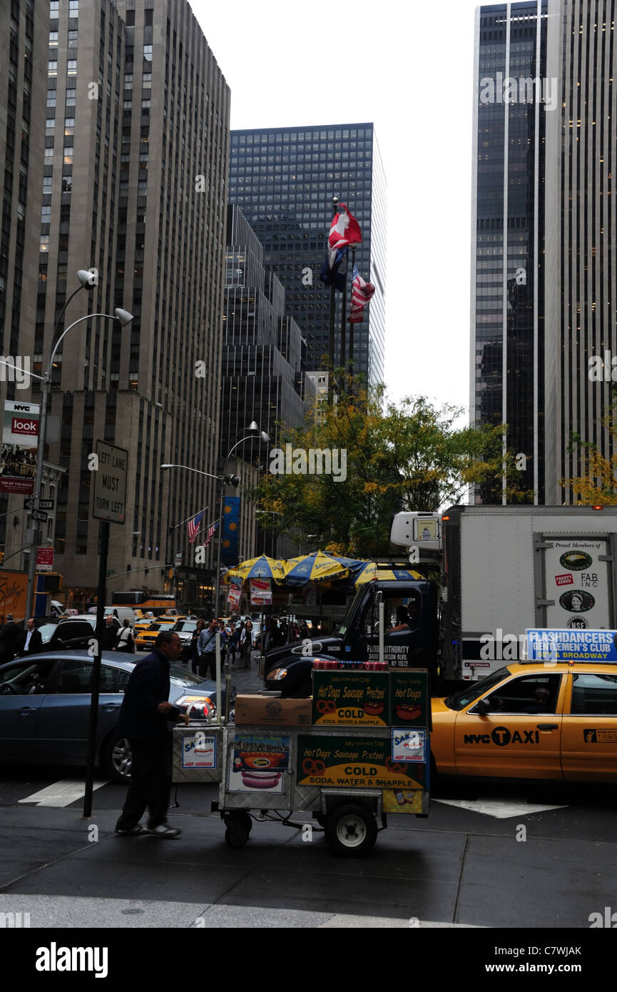 Straßenhändler, die zu Fuß mobile Snack stand, vorbei an gelbes Taxi unter Wolkenkratzern, Bürgersteig 50th Street 6th Avenue Junction, New York Stockfoto