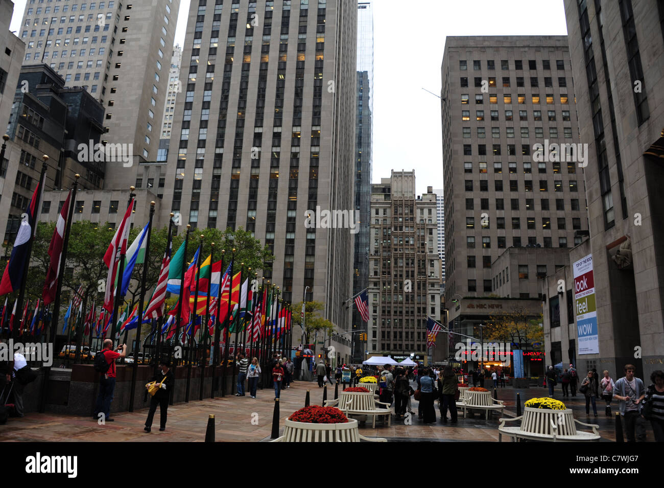 Herbstliche Ansicht, vorbei an blühenden Beeten und multi-nationalen Flaggen am Rockefeller Plaza in Richtung 49th Street NBC News-Studio, New York Stockfoto