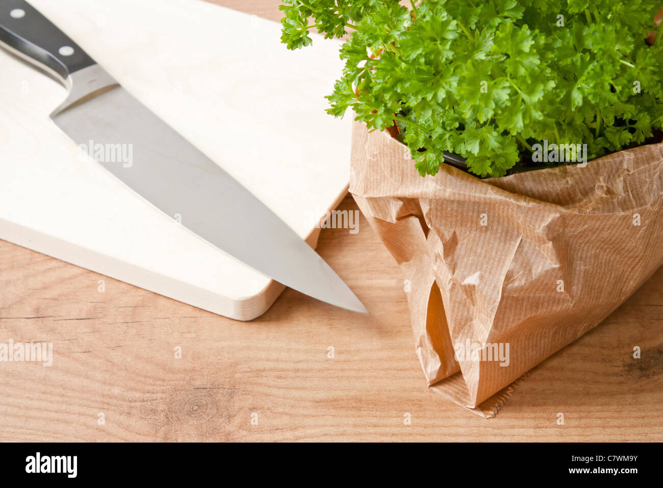 Topf mit frischer Petersilie und einem Küchenmesser auf einem Holzbrett. Stockfoto