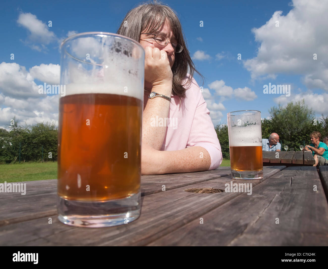 Nachdenkliche Frau in einem Biergarten an einem sonnigen Tag mit halb volle Gläser Bier auf dem einfachen Holztisch Stockfoto