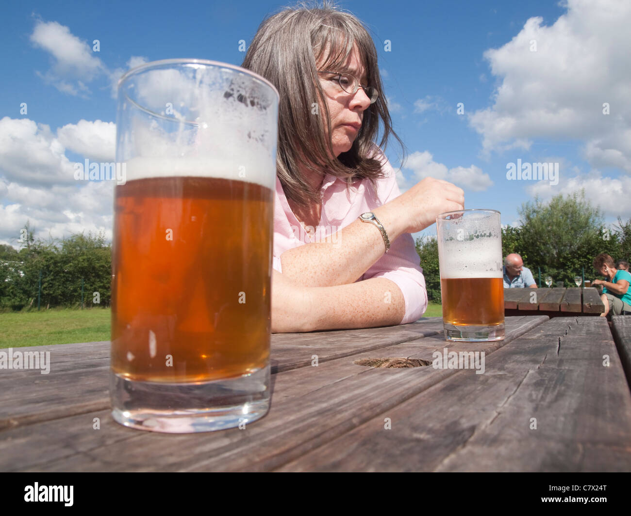 Nachdenkliche Frau in einem Biergarten an einem sonnigen Tag mit zwei halbvolle Gläser Bier auf der Ebene Holztisch Stockfoto
