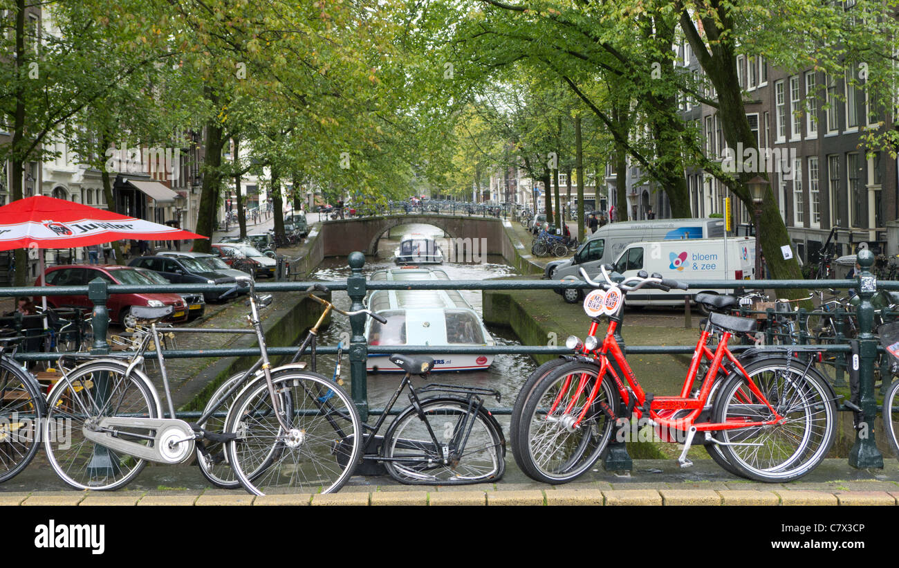 Fahrrad mit beschädigten Rad und Reifenpanne vor Kanal mit Ausflugsschiff, Amsterdam, Niederlande Stockfoto