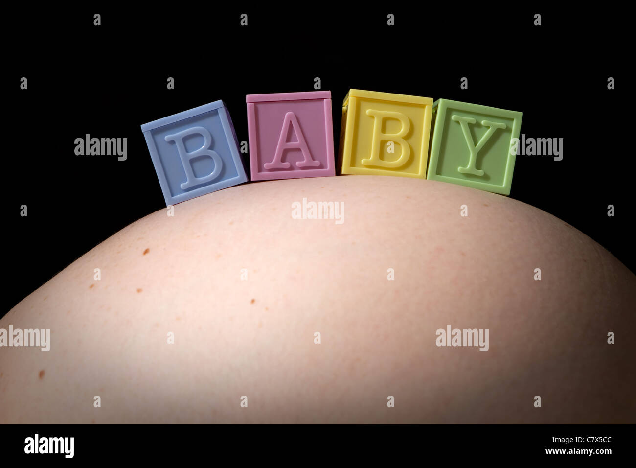 Vier bunte Buchstaben Baby Blocks buchstabieren das Wort BABY wie sie auf geschwollenen Bauch einer schwangeren Frau sitzen. Stockfoto