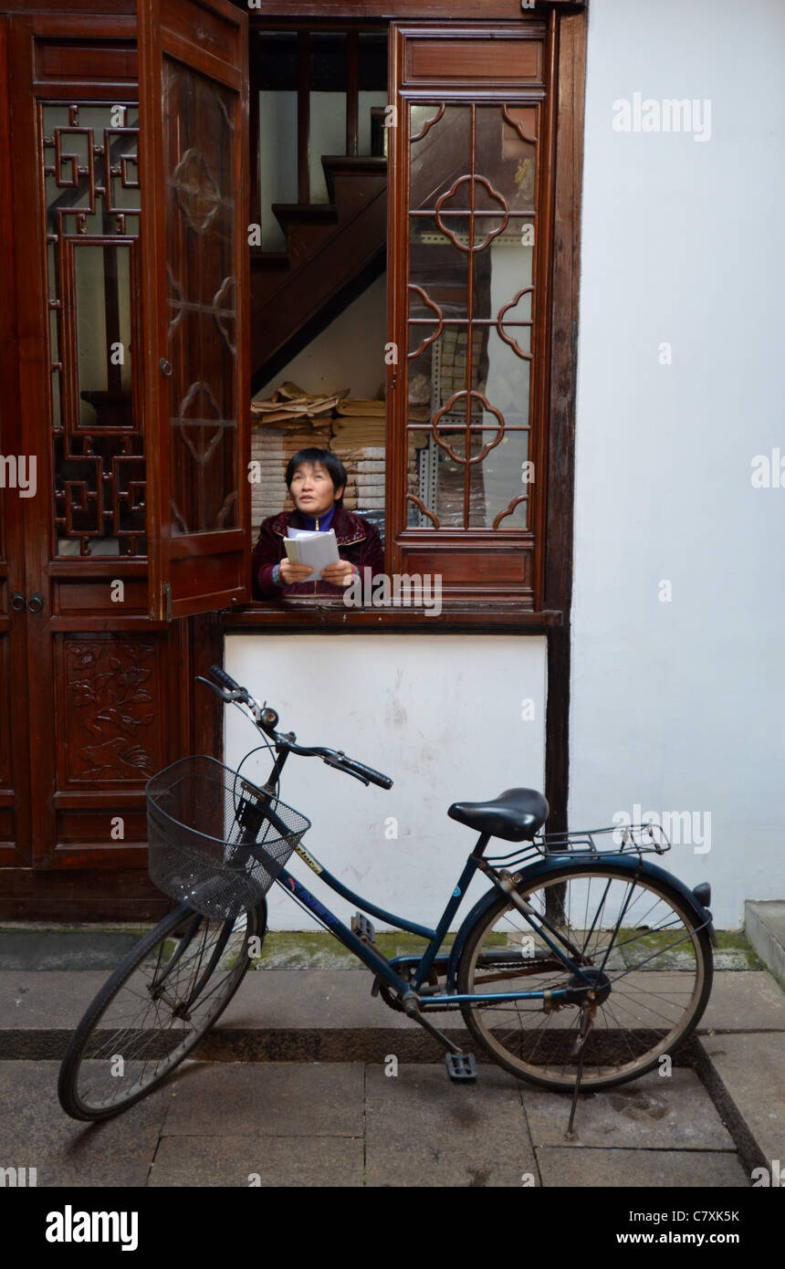 Ein Fahrrad auf einem Ständer als Frau ruft ein Kollege in einem Innenhof in QiBao Ancient Town. Stockfoto
