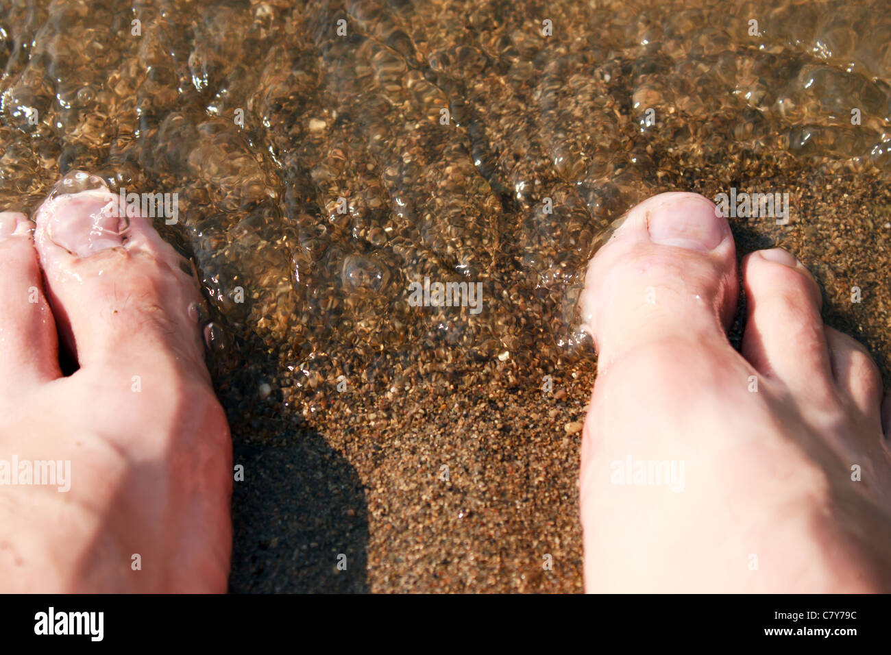 Mannes Füßen im Strandsand als flache Welle angespült wird Stockfoto