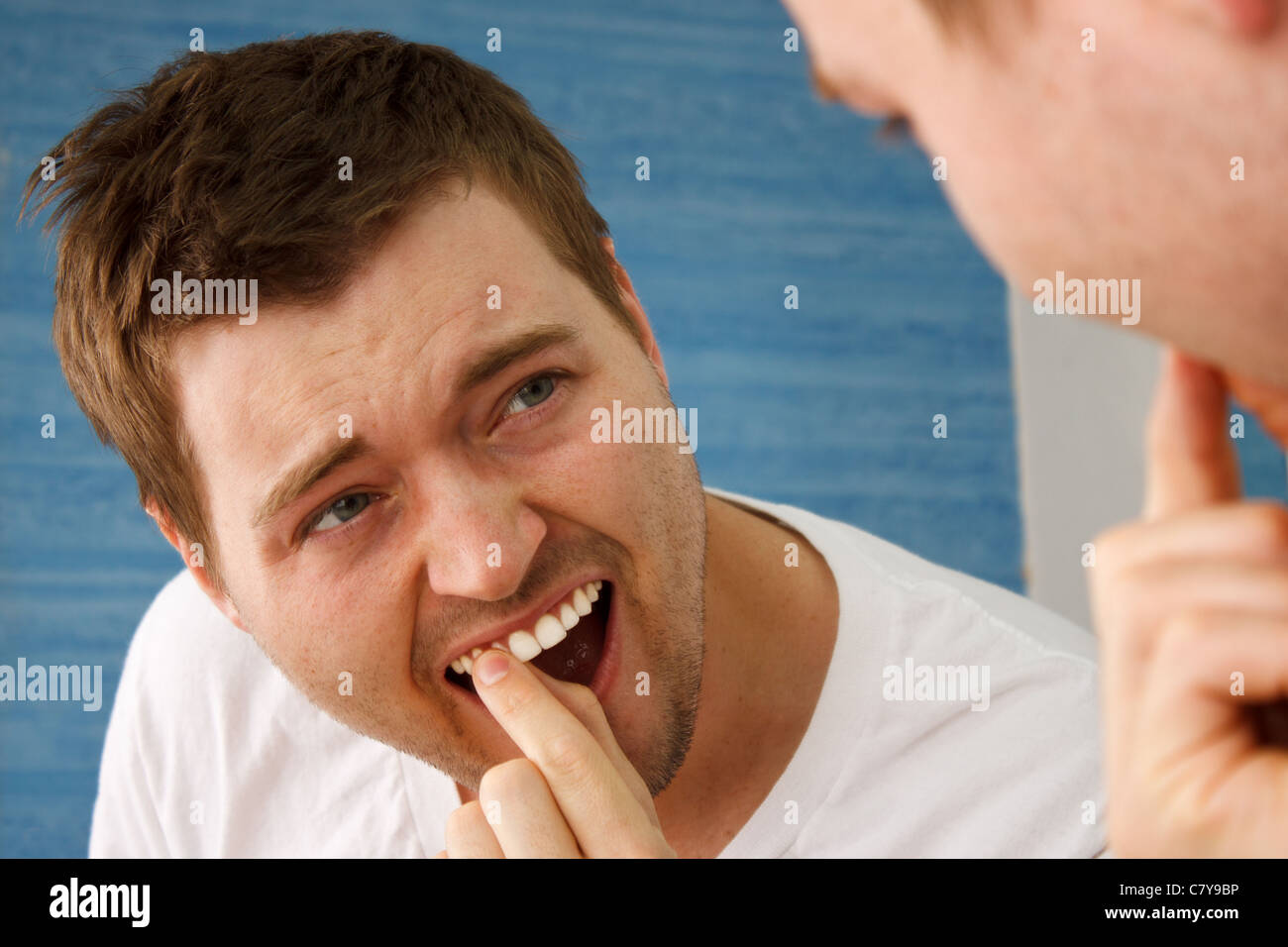 Junger Mann im weißen T-shirt Überprüfung Zähne im Spiegel Stockfoto