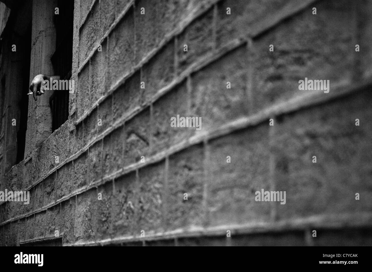 Eine Hand Rauchen einer Zigarette durch die Gitterstäbe eines Fensters. Sieht aus wie ein Gefängnis oder Jail (Gefängnis), aber nicht. Erhöhten gemauerte Wand. Stockfoto