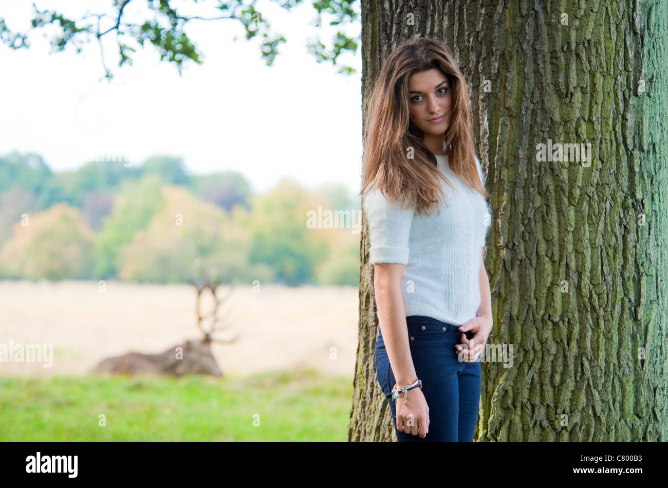 Hübsche junge 15 Jahre altes Mädchen mit langen Haaren posiert im Park und lächelnd neben einem Baum mit schöner Rinde. Stockfoto