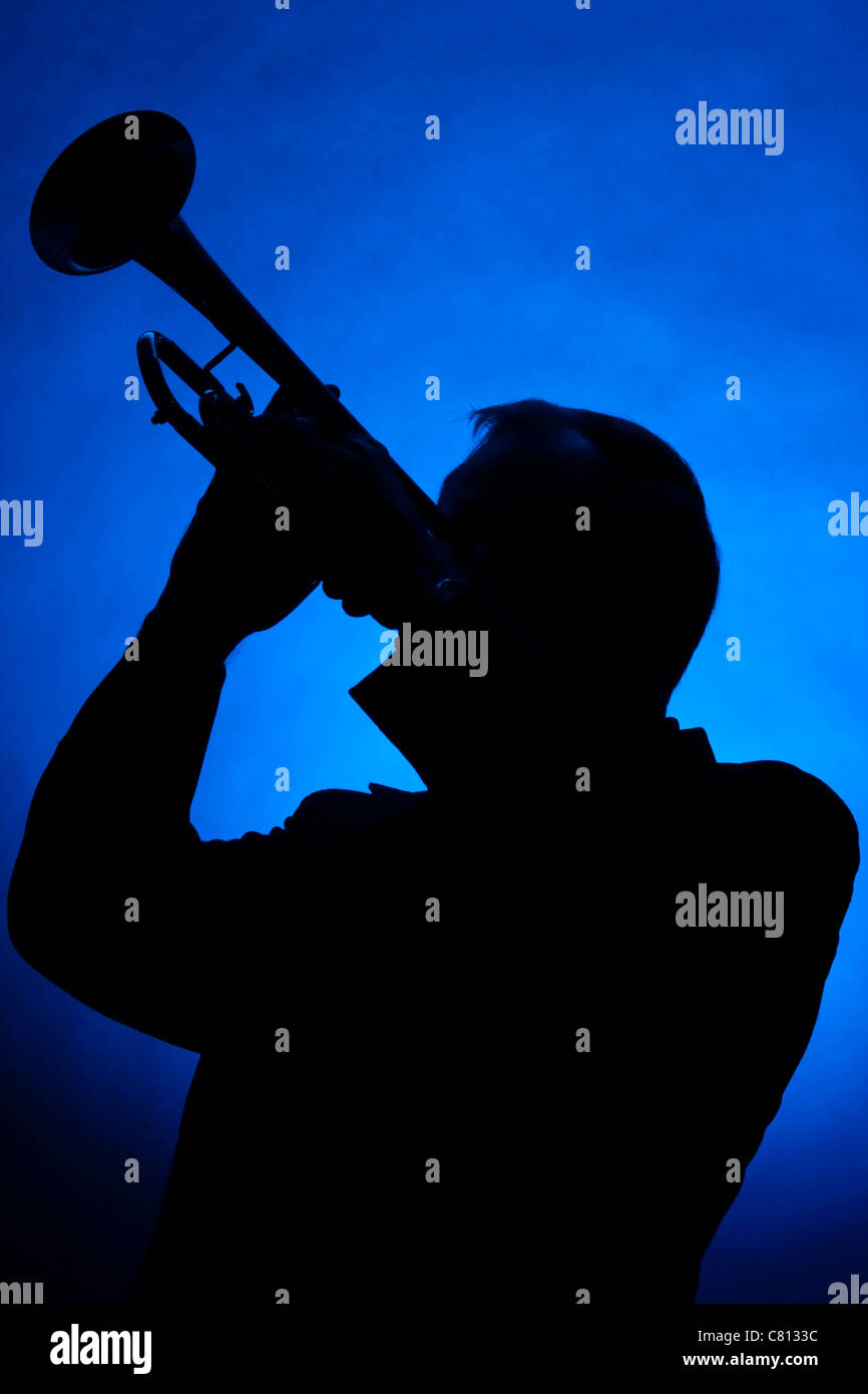 Eine Silhouette der Trompeter isoliert gegen einen blauen Scheinwerfer im vertikalen Format. Stockfoto