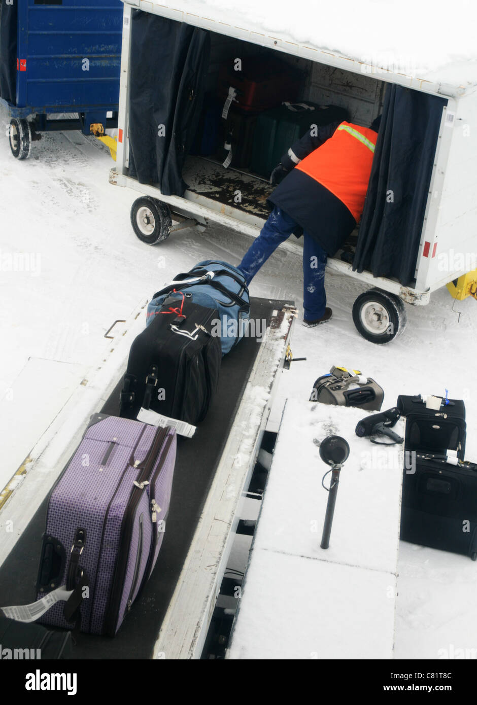 eine Fluggesellschaft Bagagiste laden Gepäck aus einem Wagen auf ein Förderband an einem kalten, grauen Schneetag Stockfoto